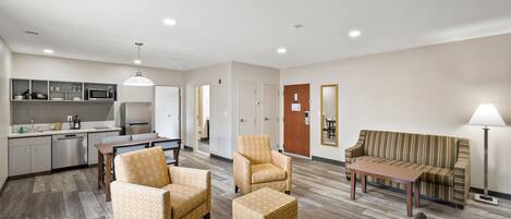 A modern hotel room with a kitchenette, a sofa, a dining table, and a chair.