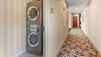 Un pasillo de hotel con una lavadora, piso alfombrado y una puerta que indica 'Guest Lounge'.