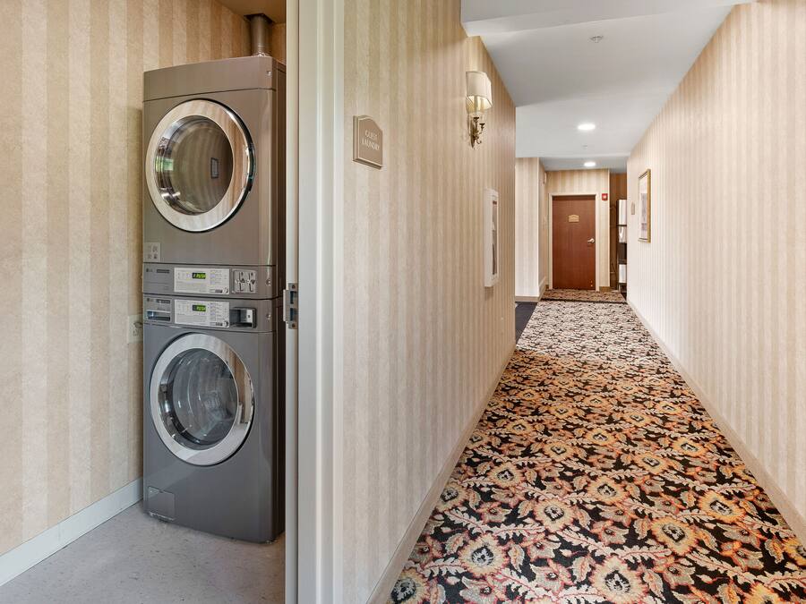 Un pasillo de hotel con una lavadora, piso alfombrado y una puerta que indica 'Guest Lounge'.
