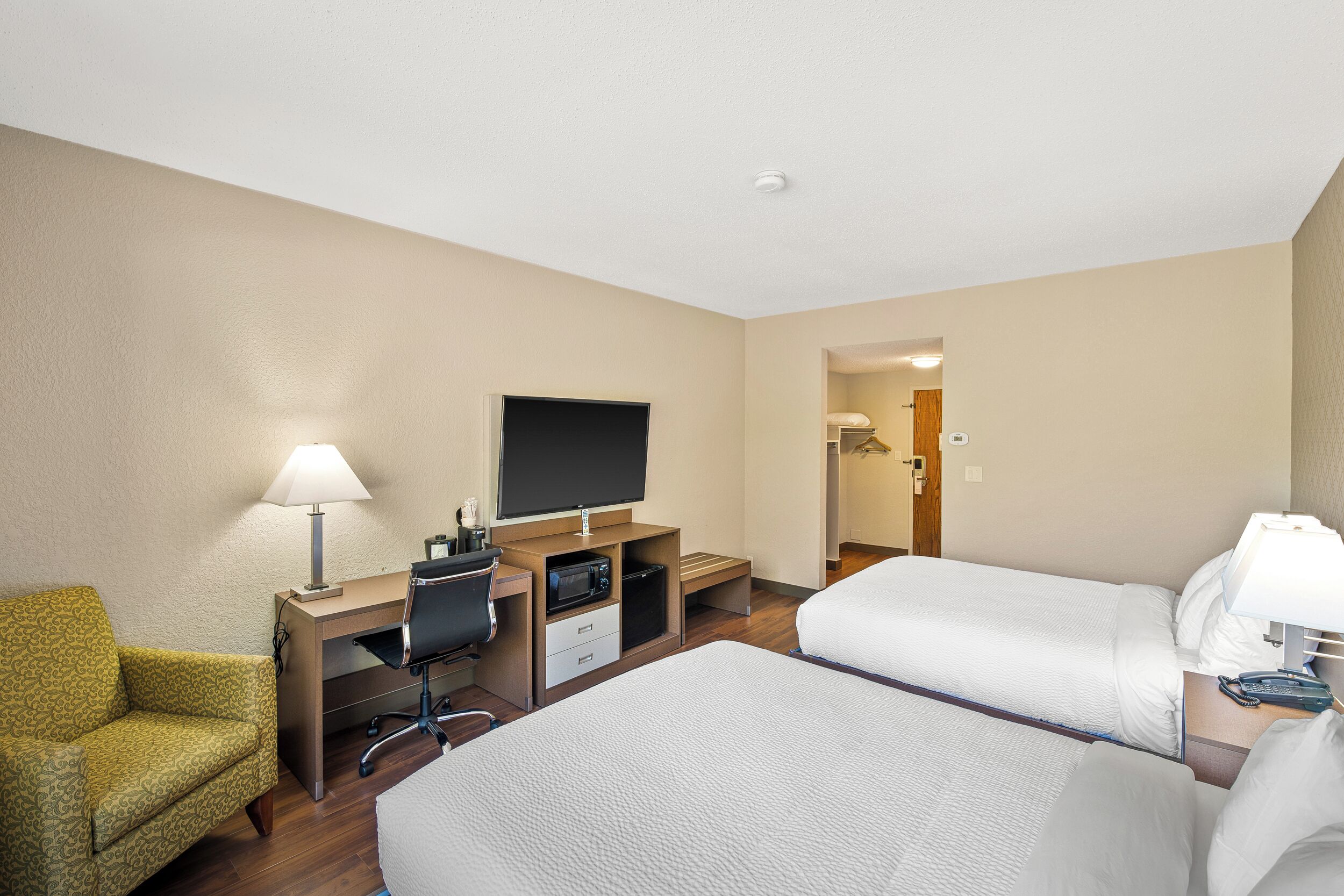 A hotel room with two beds, a desk with a computer, a TV, and a chair.