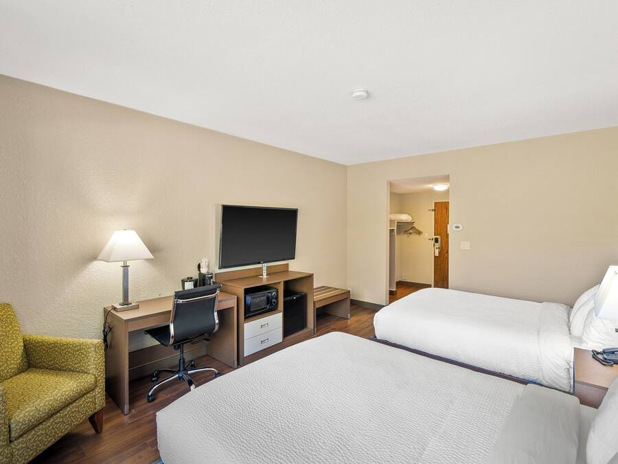 Una habitación de hotel con dos camas, un escritorio con computadora, un televisor y una silla.