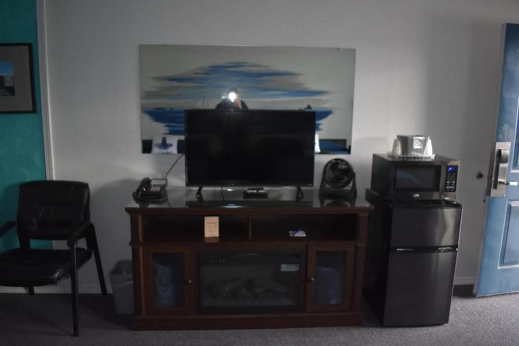 Una habitación con televisión, un refrigerador pequeño, un armario y una silla.