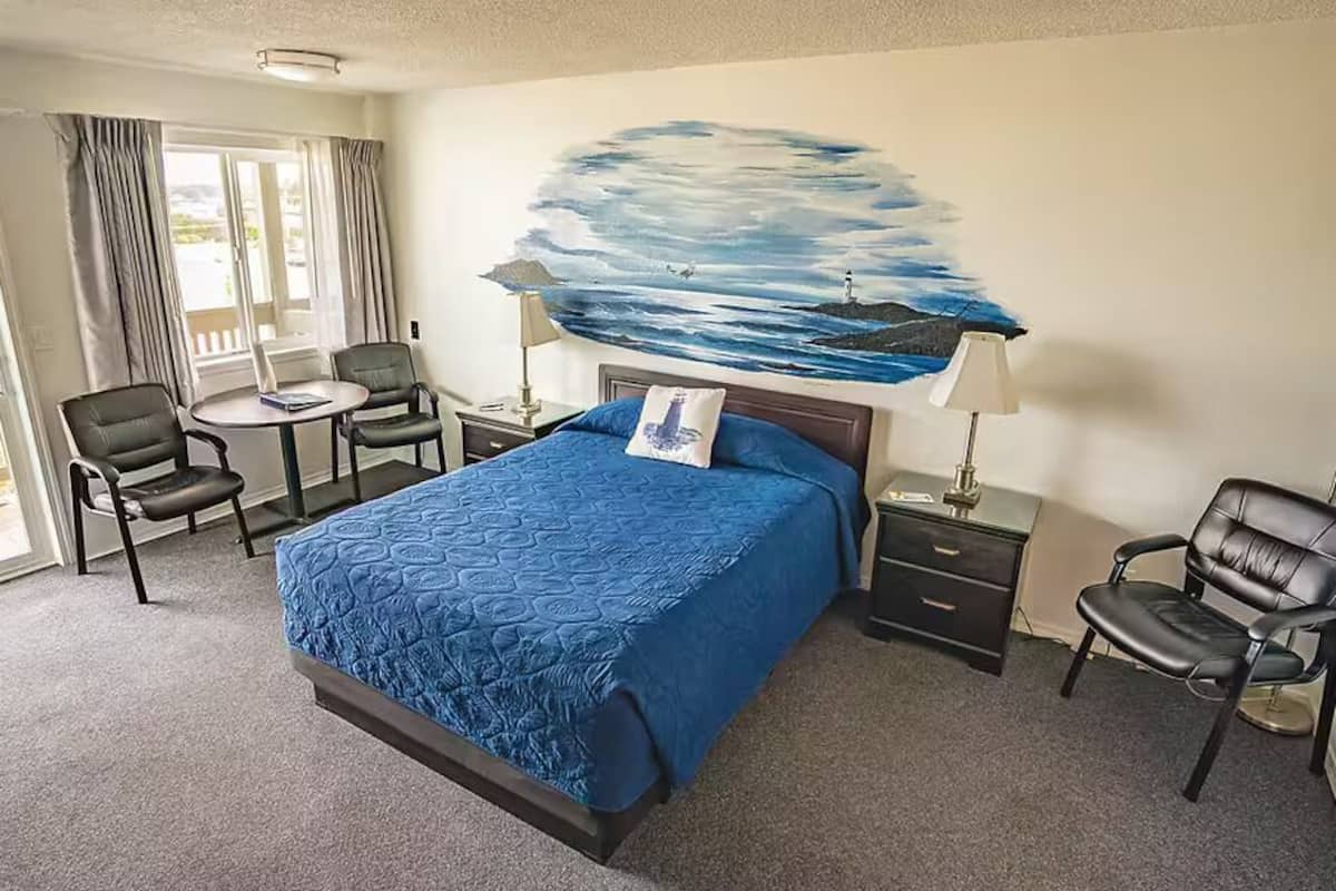 Habitación de hotel con una cama grande, un escritorio, dos sillas, un cuadro marino y vistas al exterior.