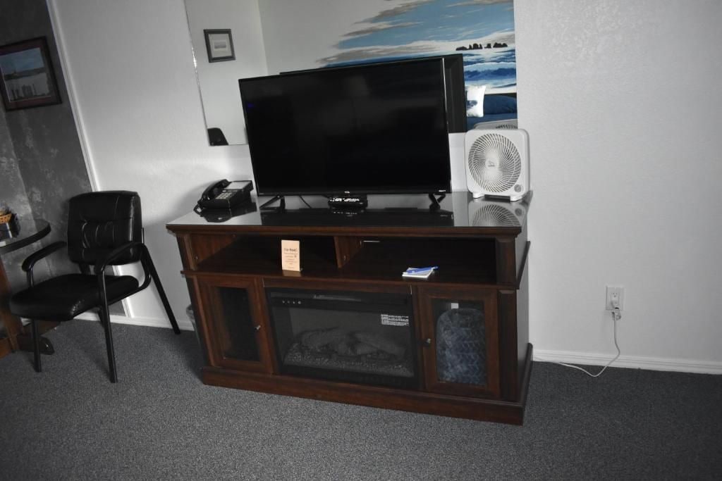 A room with a television on a wooden stand, a white fan, and a black chair.