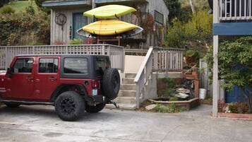 Ein rotes Geländefahrzeug parkt vor einem Haus mit einer Holzterrasse und einer Treppe, die zu einer Veranda führt.