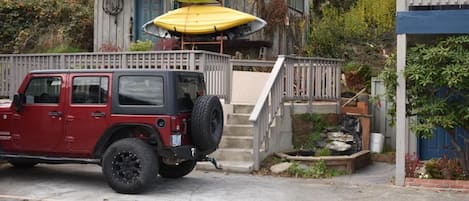 A red off-road vehicle parked in front of a house with a wooden deck and a set of stairs leading to a porch.