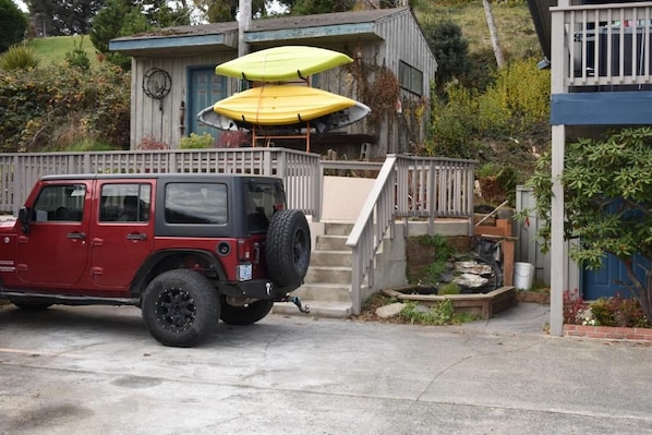 Un vehículo todoterreno rojo estacionado frente a una casa con terraza de madera y un conjunto de escalones que conducen a un porche.