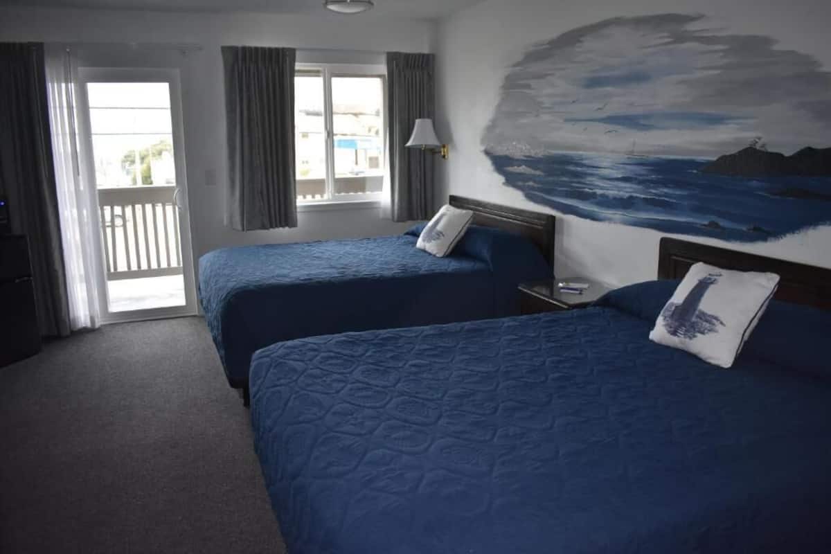 Habitación de hotel con dos camas, un cuadro de paisaje marino, un balcón con cortinas y vistas al exterior.