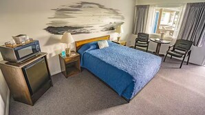 A hotel room with a bed, a desk, a chair, a TV, and a painting on the wall.