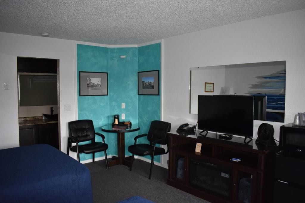 A hotel room with a bed, a desk with a computer, a television, and two chairs.