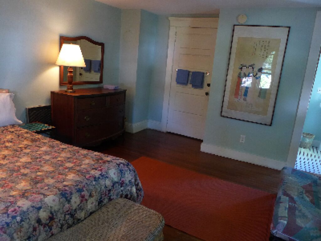 A bedroom with a bed, dresser, mirror, and a door with towels hanging on it.