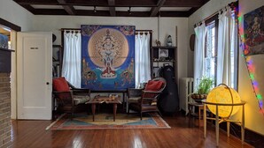 Une pièce décorée d’une grande tapisserie, comprenant deux fauteuils en osier, une petite table et une lampe en forme de globe terrestre.