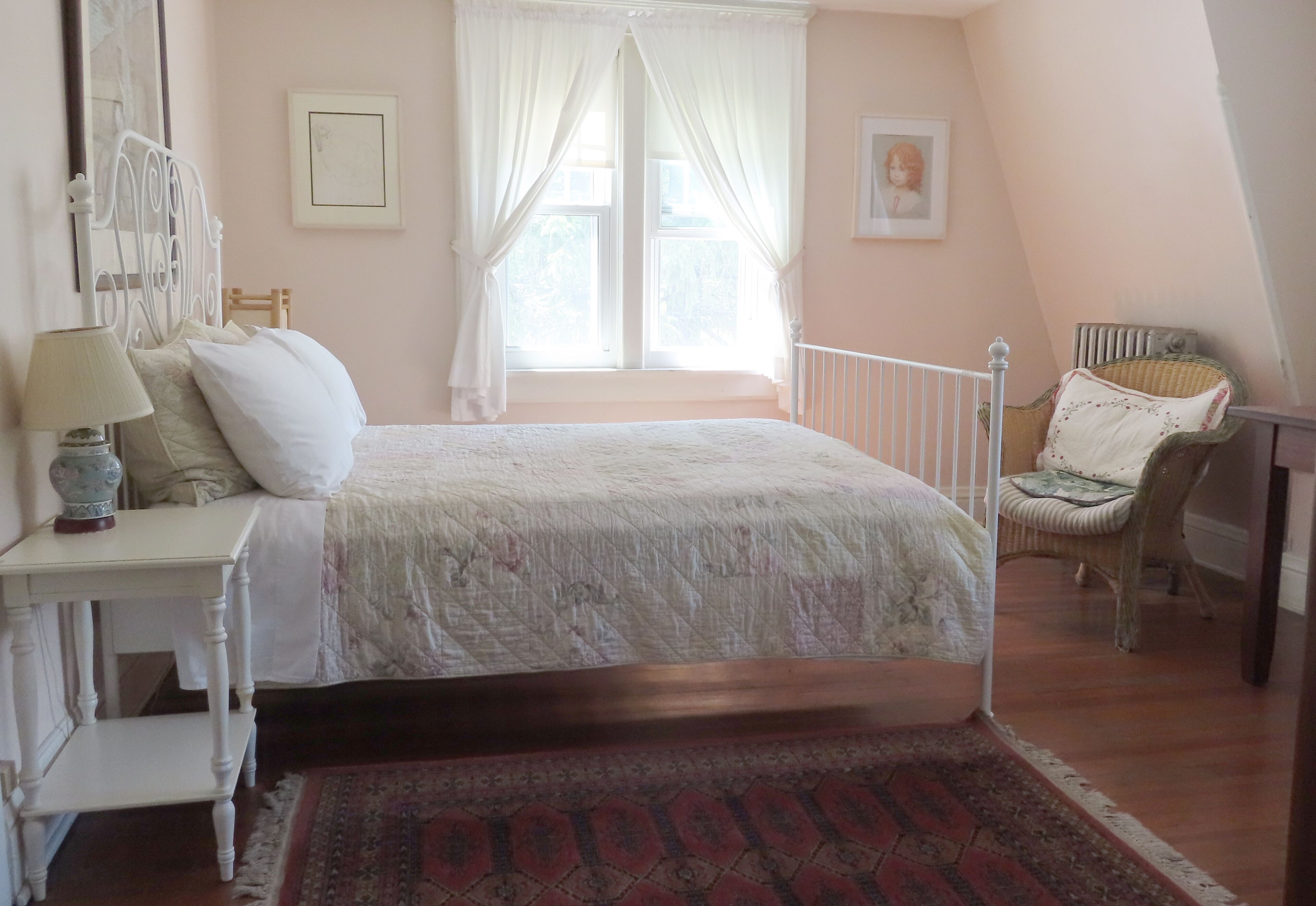 Une chambre à coucher avec un lit, une table de chevet, une lampe, une chaise et une fenêtre avec des rideaux.
