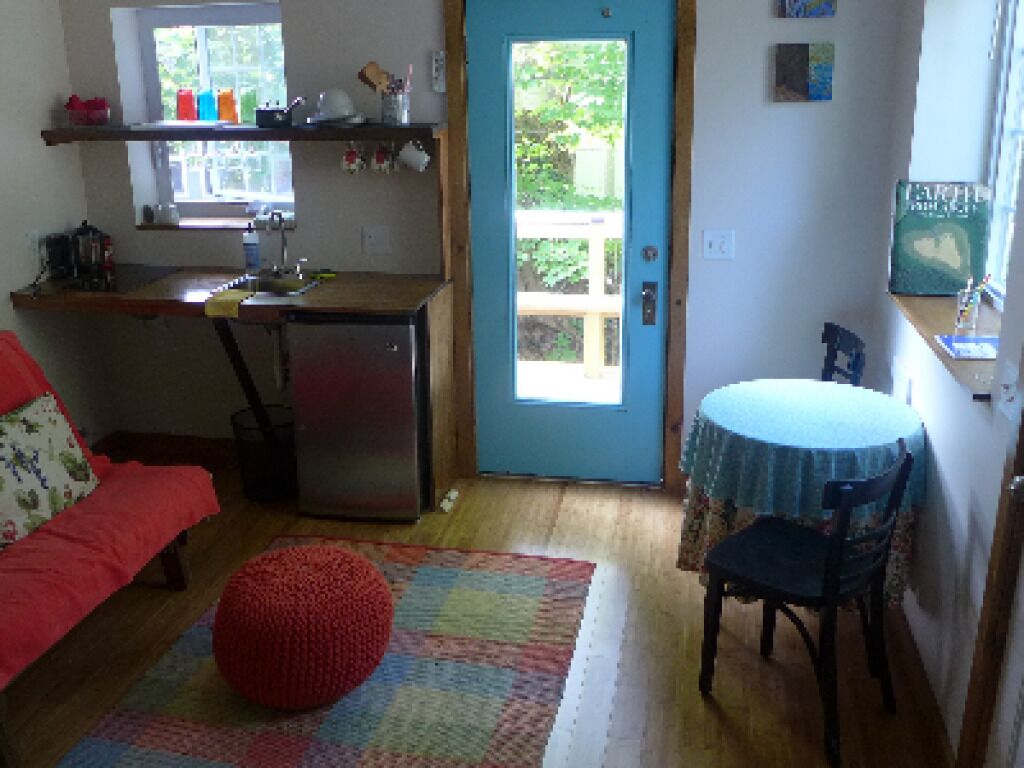 Cocina compacta con refrigerador, un lavamanos y una ventana sobre la puerta. Hay una zona de comedor con una mesa redonda y una silla.