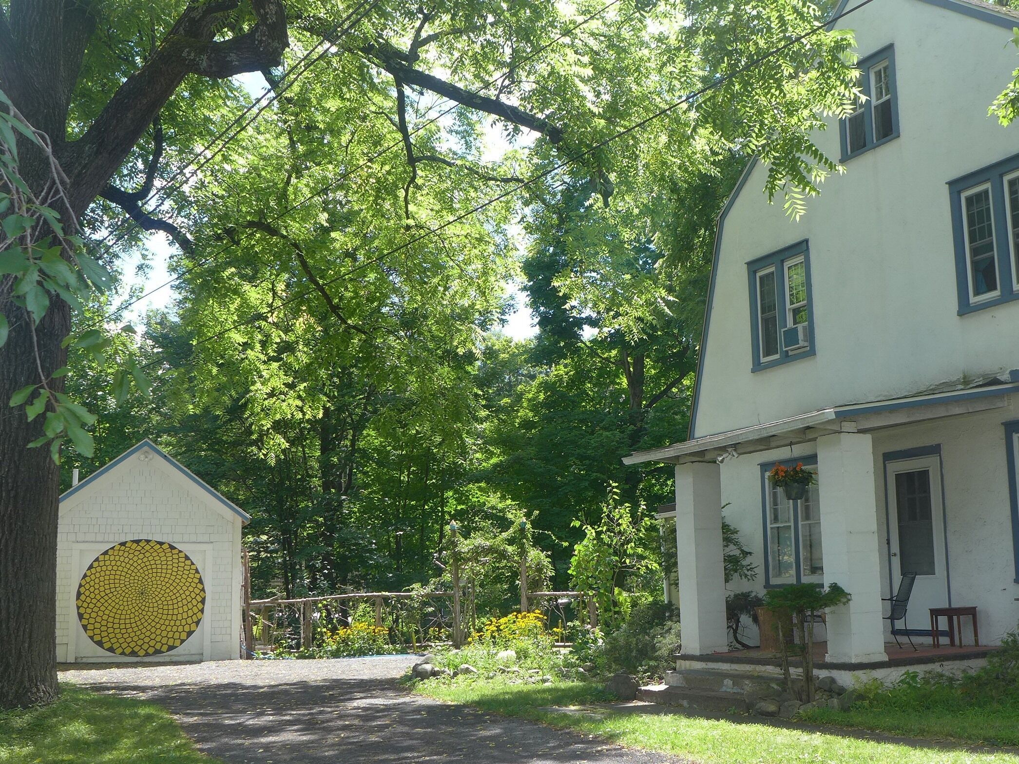 A white building with a large circular mosaic on the front wall, surrounded by lush greenery and trees.