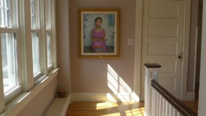 Un couloir avec un portrait encadré accroché au mur, une porte sur la droite et une fenêtre sur la gauche.