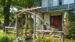 Une pergola en bois rustique dans un jardin, avec une maison en arrière-plan.