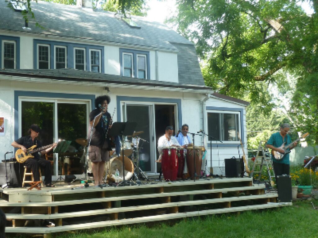 Una banda tocando en un escenario de madera frente a una casa con porche.
