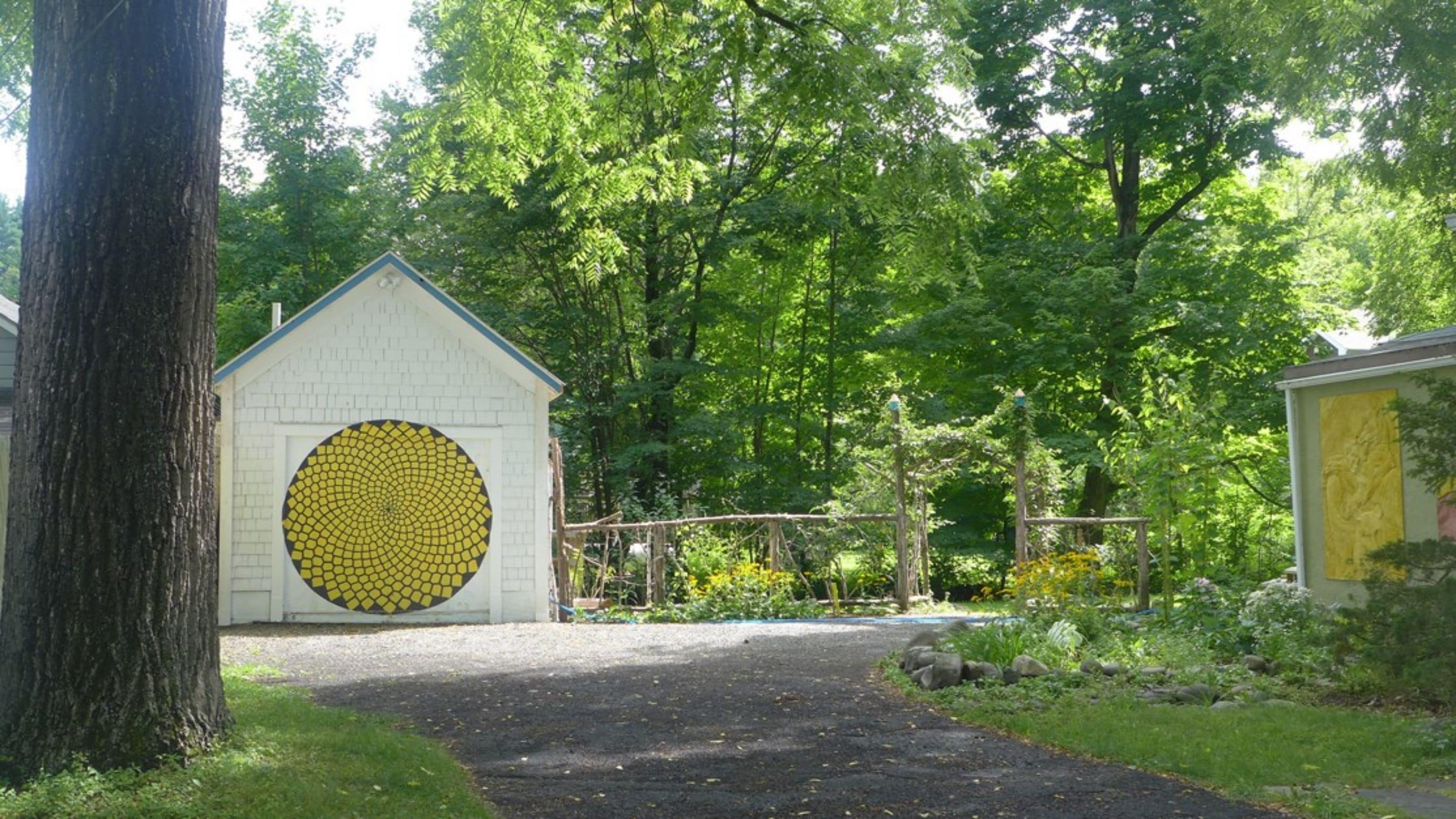 Un bâtiment doté d’une grande fenêtre en mosaïque circulaire, entouré d’arbres et bordé d’un chemin de gravier.