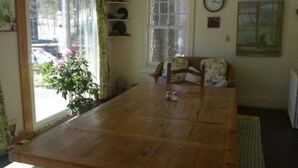 Un espace repas comprenant une table en bois, des chaises, un lustre et une vue sur l’extérieur grâce à de grandes fenêtres.