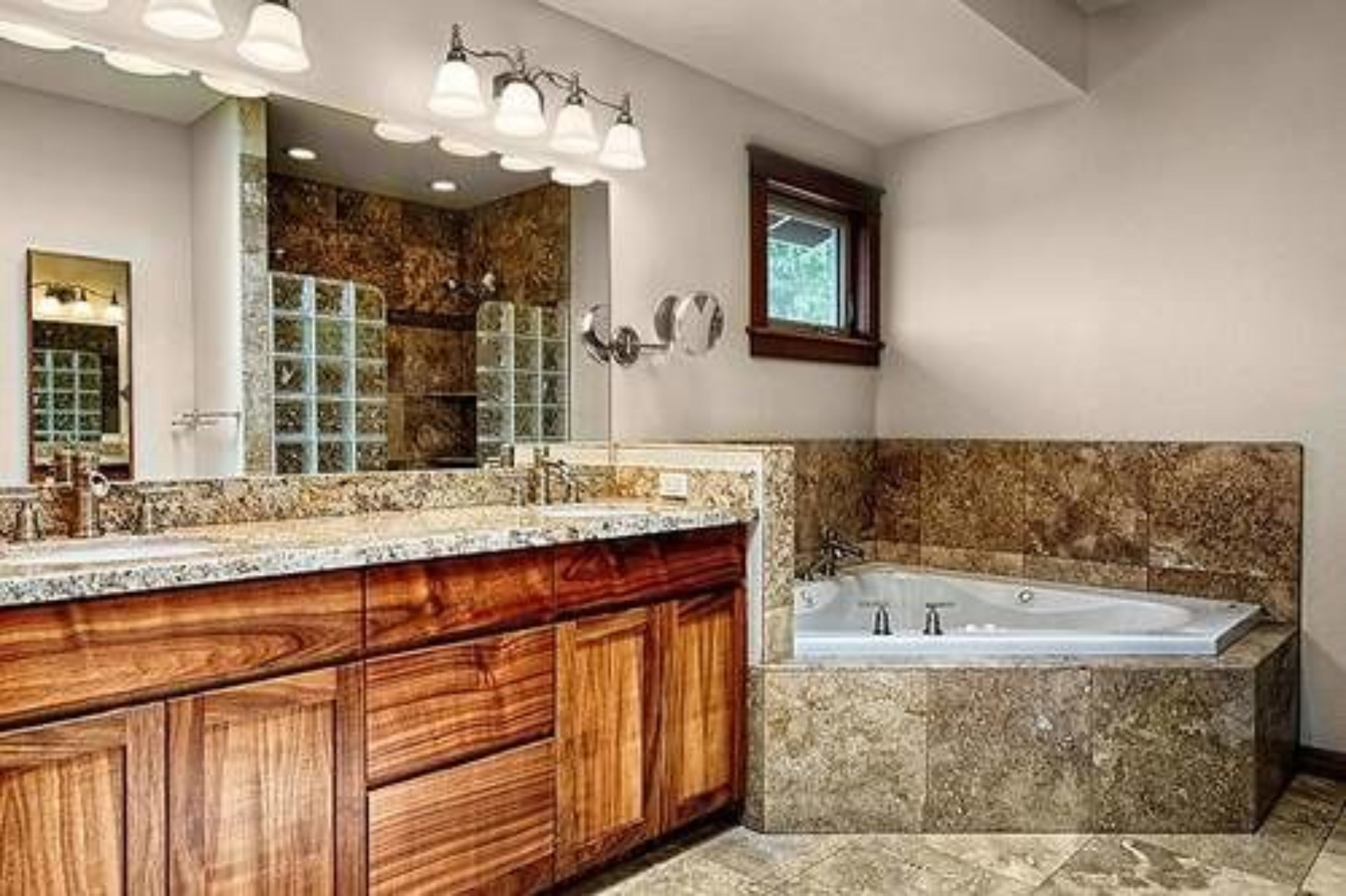 Un baño con un mueble de tocador de madera grande, una bañera independiente y un espejo amplio con iluminación.
