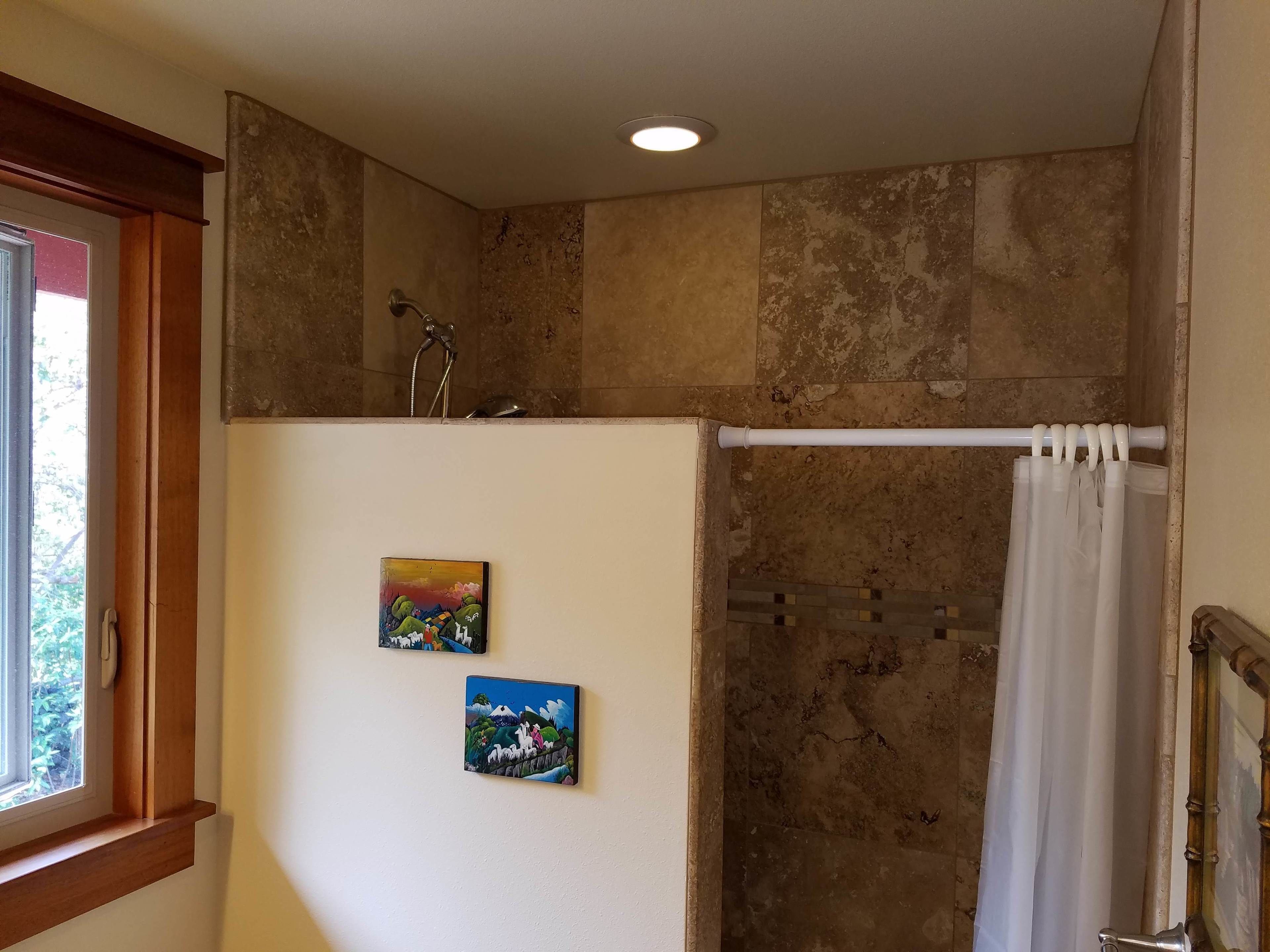 Un bagno con doccia, una finestra e due quadri appesi al muro.