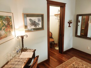 A room with a wooden floor, a dining table with chairs, a framed butterfly artwork, a mirror, and a door leading to another room.