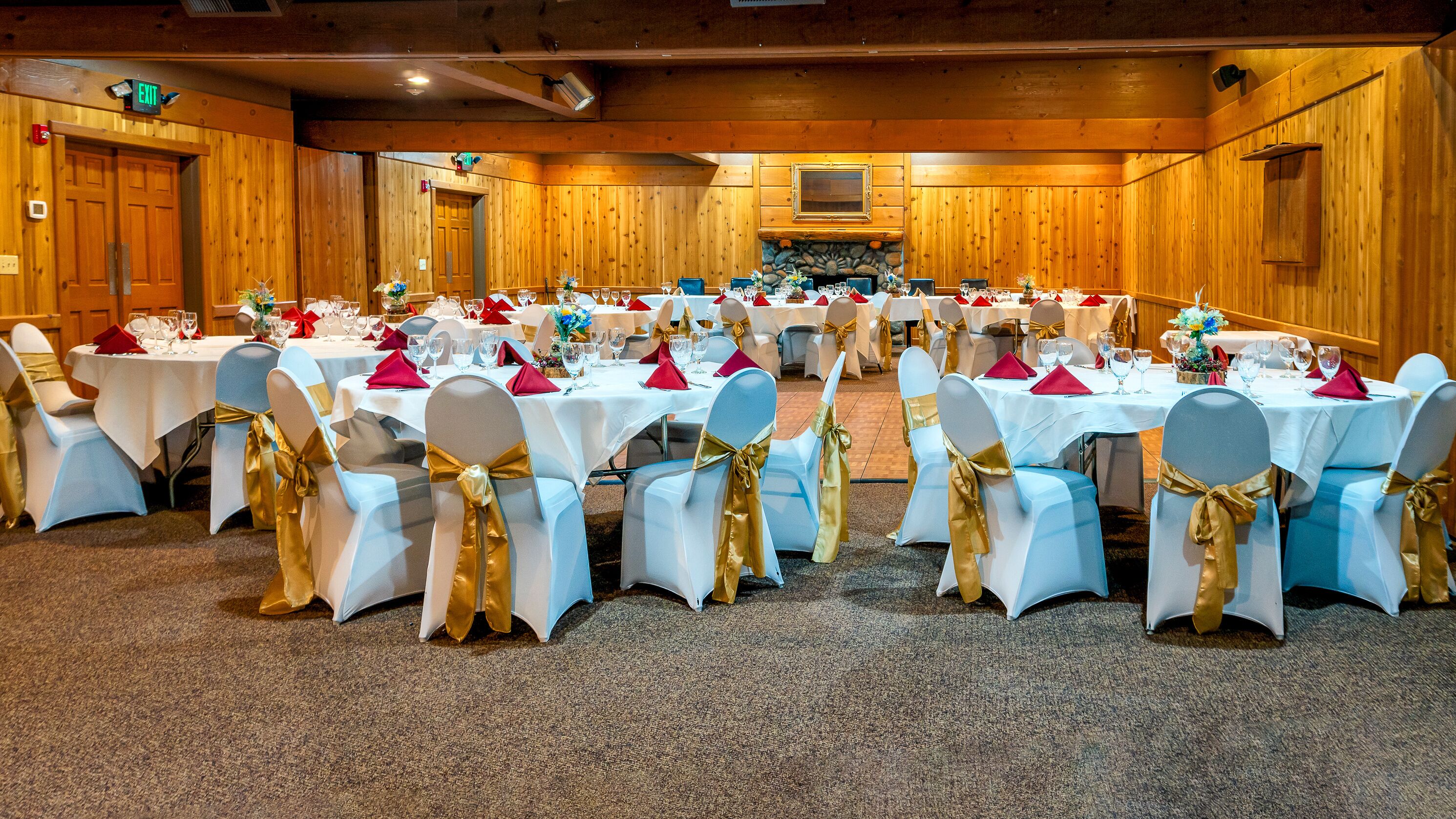 A banquet hall with multiple round tables set for a formal event, featuring white tablecloths, gold sashes, and red napkins.