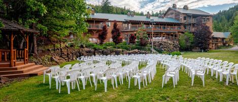 A lodge with a circular outdoor seating area arranged in rows of white plastic chairs, surrounded by a well-maintained lawn and a stone retaining wall.