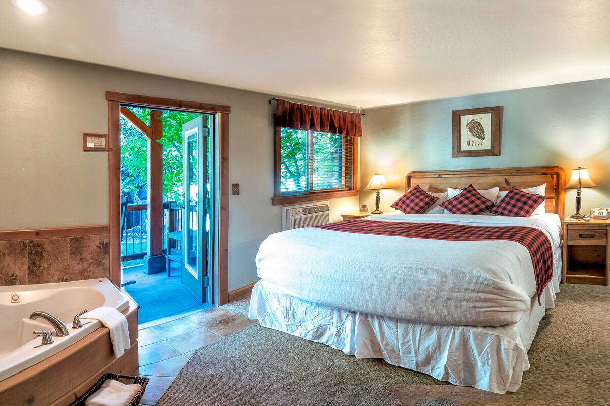 A hotel room with a large bed, a separate bathroom with a bathtub, a window with curtains, and a view of the outdoors.