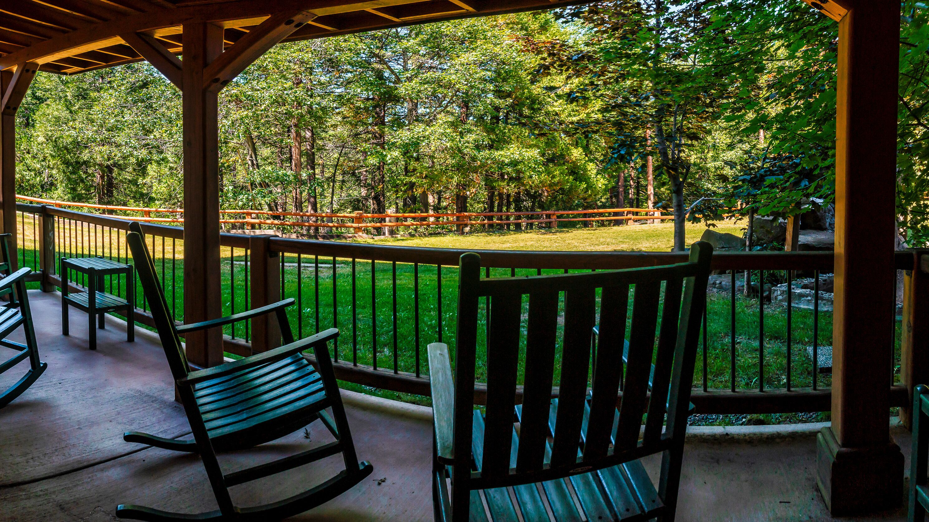 A covered outdoor area with wooden benches and a railing overlooking a grassy park with trees.