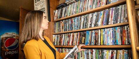 A person in a yellow jacket browsing a bookshelf filled with DVDs.