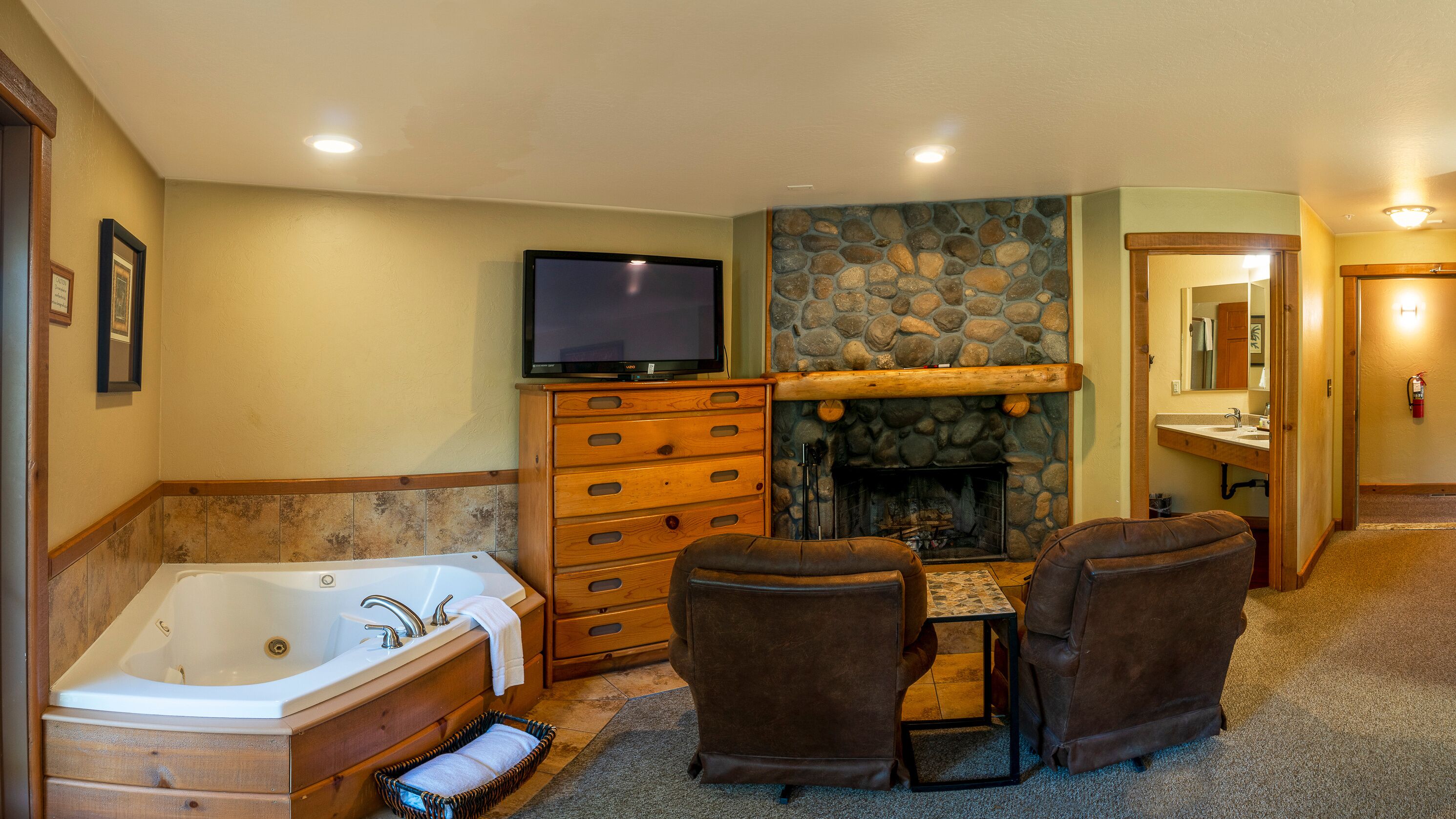 A bathroom with a bathtub, wooden cabinet, stone wall, fireplace, and a television.