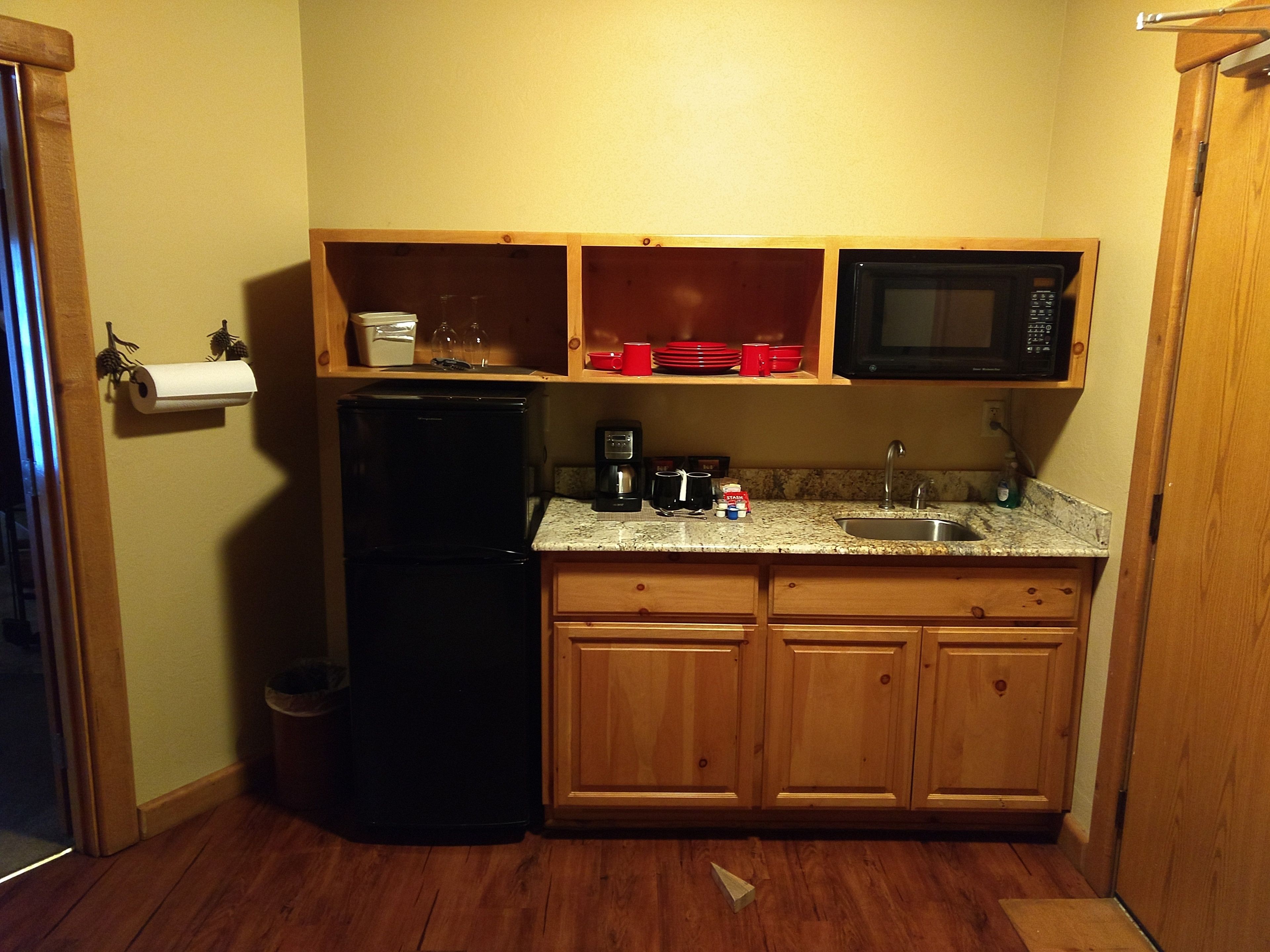 A compact kitchen with wooden cabinets, a black refrigerator, a microwave, and a granite countertop.