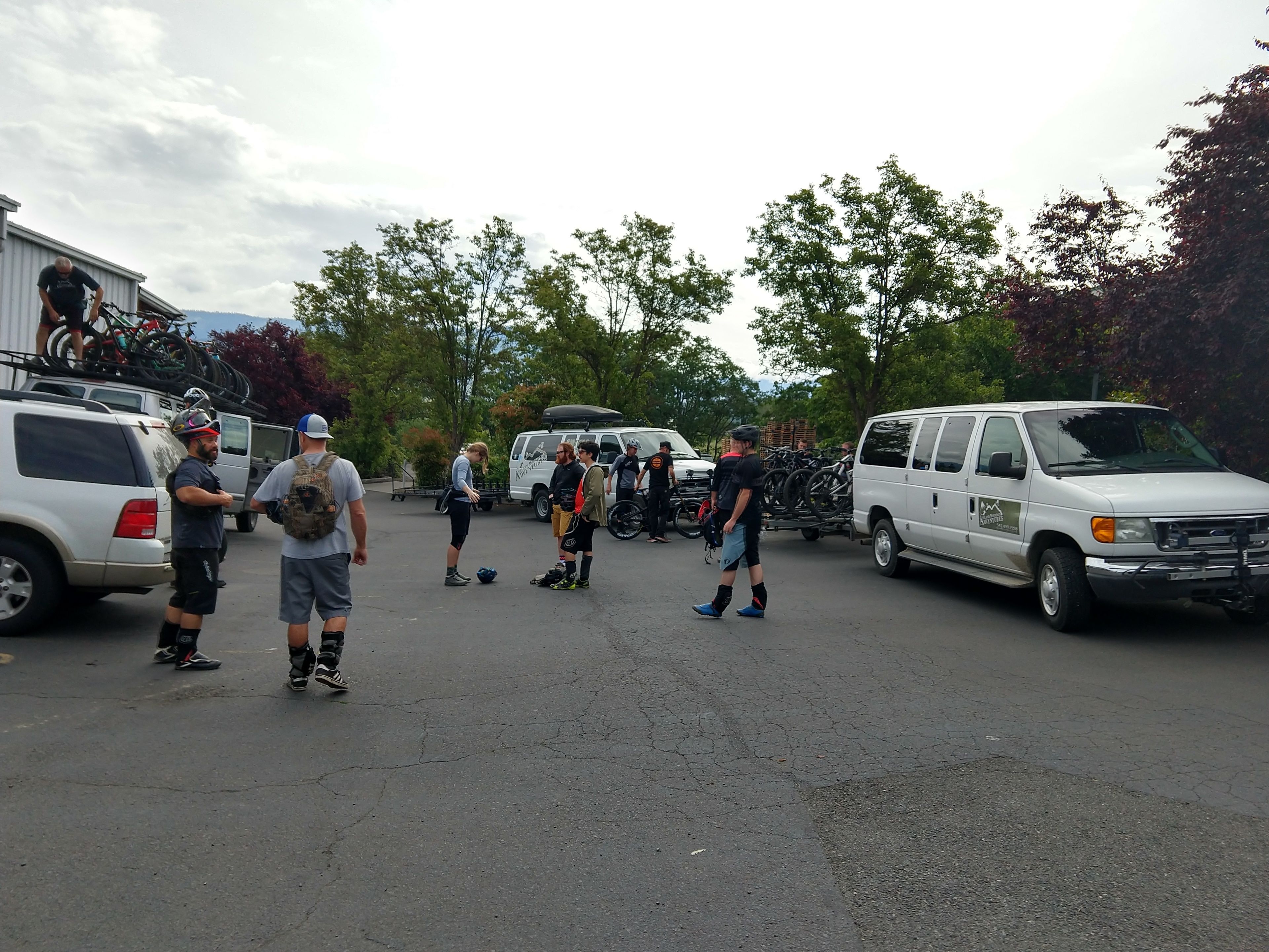 A group of people standing in a parking lot with bicycles and vans.