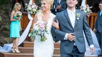 A couple walking down a grassy aisle with a gazebo in the background.