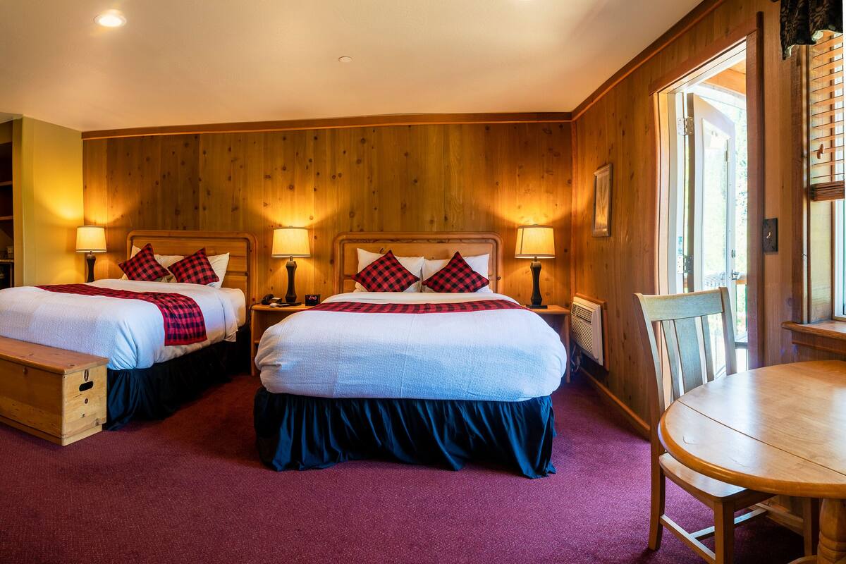 A double room with two beds, wooden paneling, a wooden bench, a table, and a window.