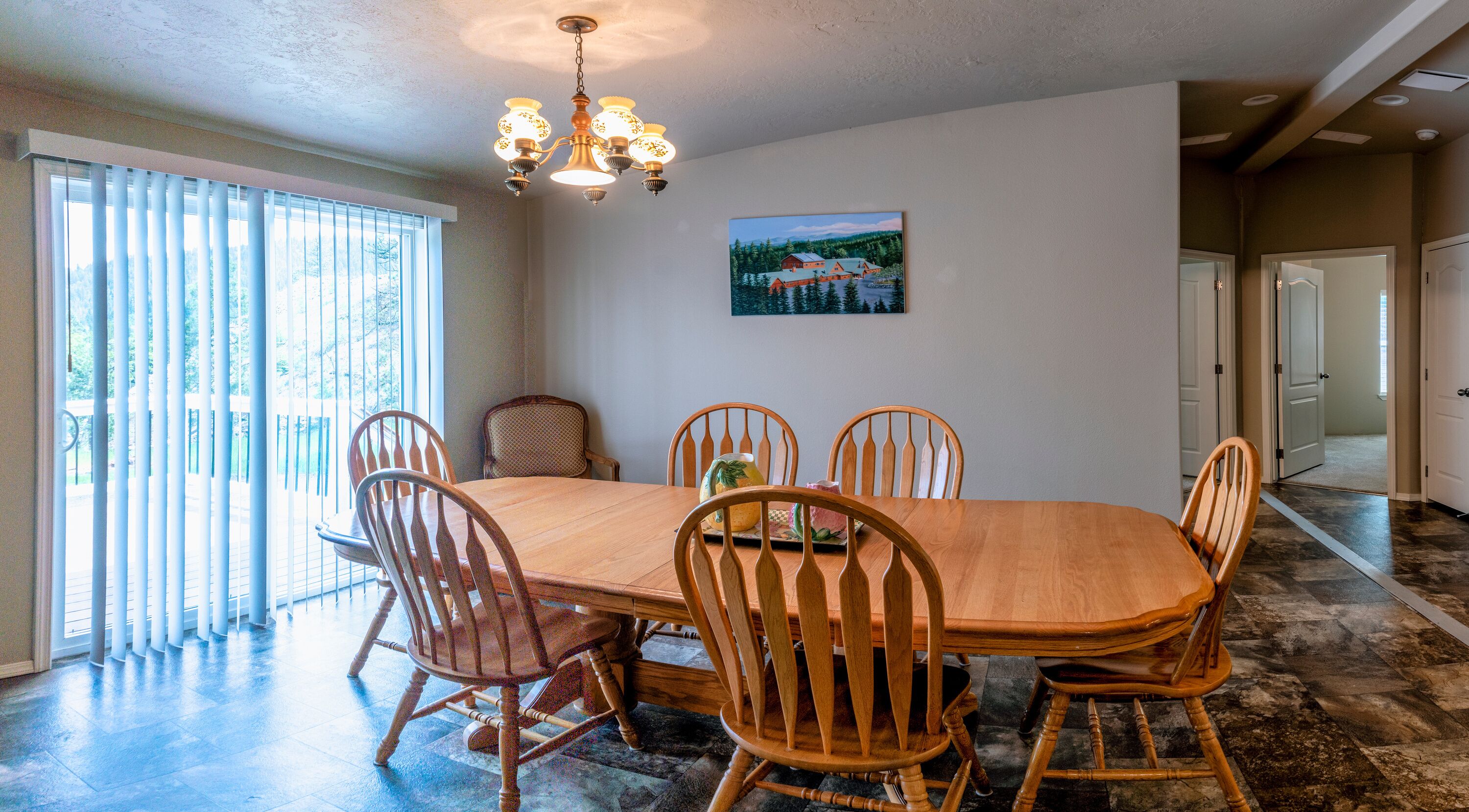 Une salle à manger avec une table et des chaises en bois, un lustre et un tableau accroché au mur.