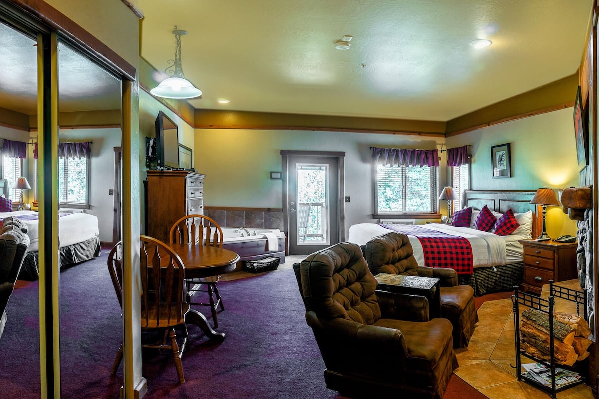A hotel room with two beds, a dining table, chairs, a fireplace, and a large mirror.