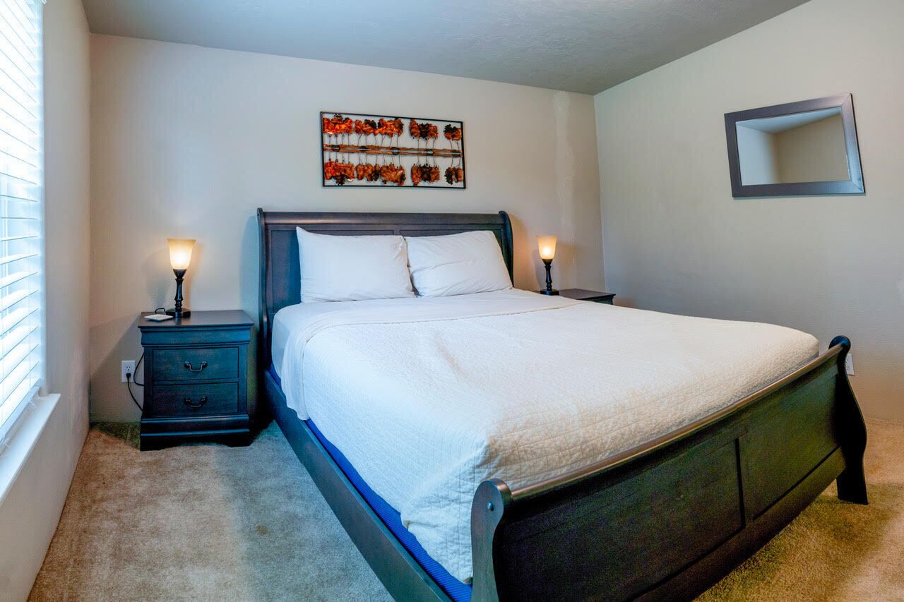 A bedroom with a bed, two bedside tables, a wall-mounted mirror, and a decorative wall piece.