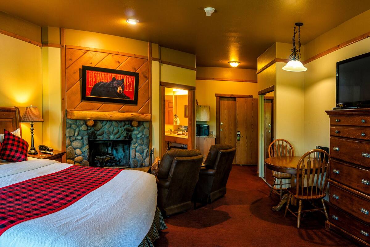A hotel room with a large bed, a fireplace, a dining area, and a television.