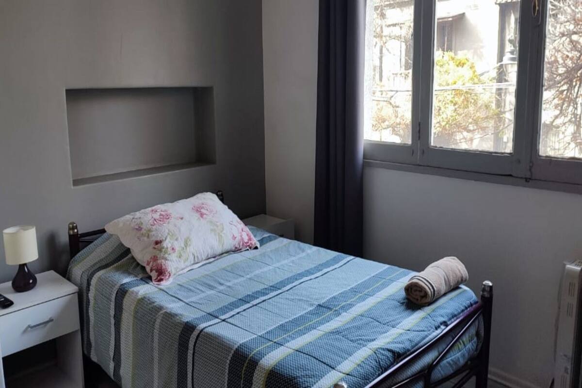 Ein Schlafzimmer mit einem Bett, einem Nachttisch, einer Lampe, einem Fenster und einer Heizung.