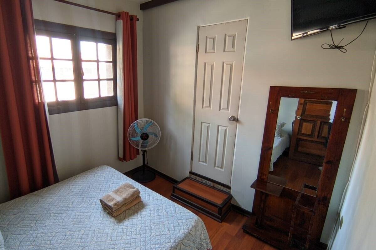 Ein Schlafzimmer mit Bett, Ventilator, Tür und Spiegel.