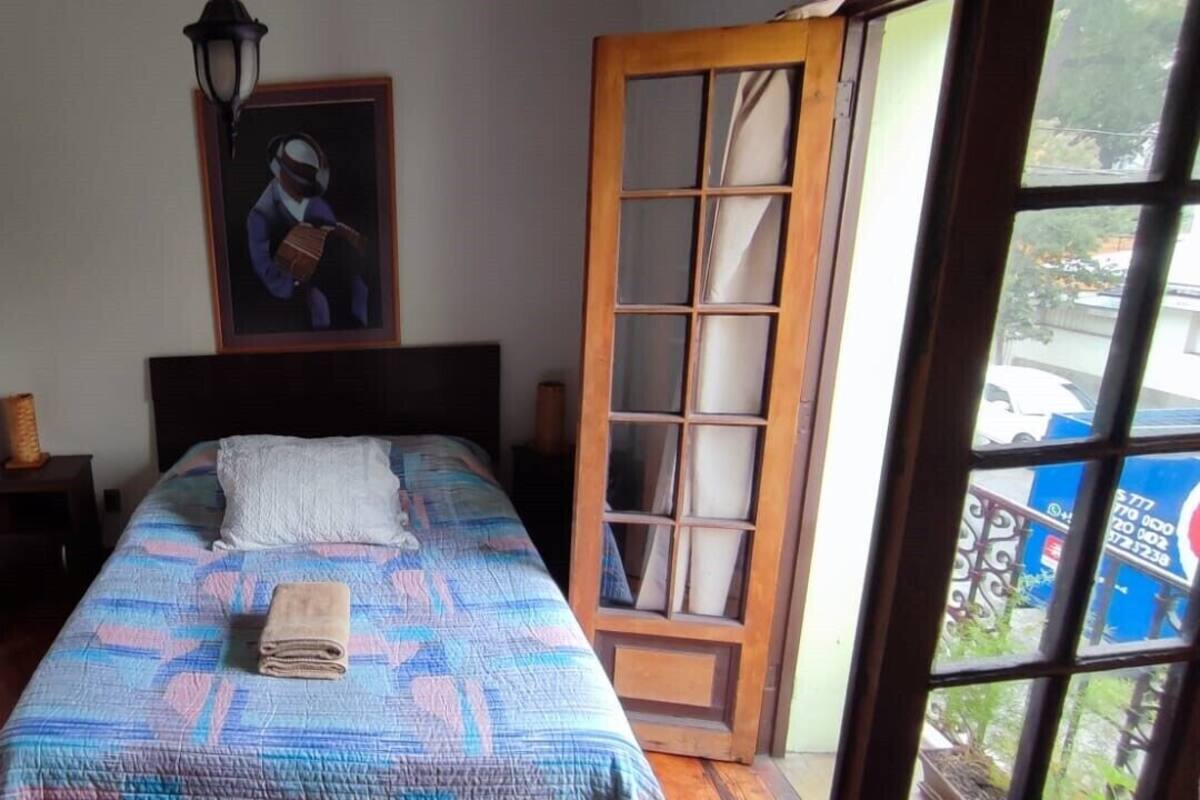 Ein Schlafzimmer mit Bett, Nachttisch, Lampe, einem Gemälde und einem Fenster mit Aussicht.