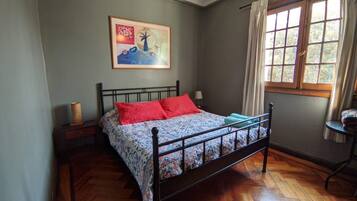 Un dormitorio con cama, un cuadro en la pared, una ventana con cortinas y una mesita de noche con lámpara.
