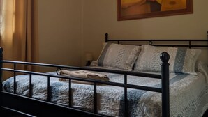 Un dormitorio con cama, mesita de noche, un cuadro en la pared y ventana con cortinas.