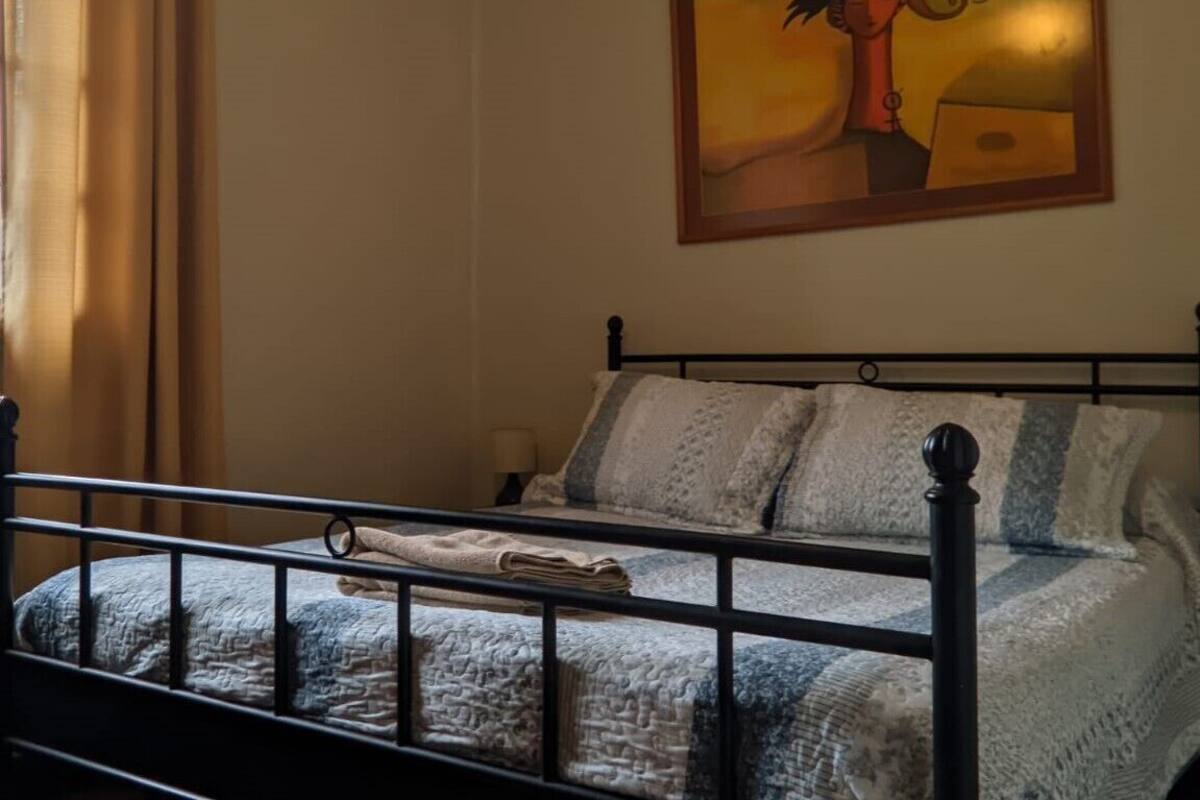 Ein Schlafzimmer mit einem Bett, einem Nachttisch, einem Bild an der Wand und einem Fenster mit Vorhängen.