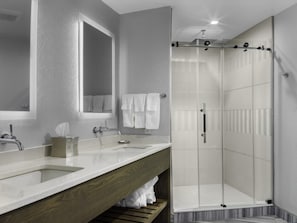 A modern bathroom with two sinks, a large mirror, and a glass-enclosed shower.