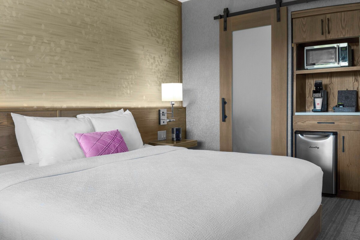 Ein Hotelzimmer mit einem großen Bett, einem Holzkopfende, einer Mikrowelle, einer Kaffeemaschine und einem Kühlschrank.