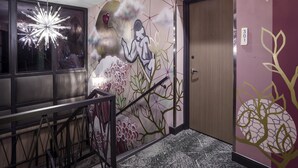 A hallway with a modern design, including a decorative wall with a mural, a staircase with a metal railing, and a door with a number sign.